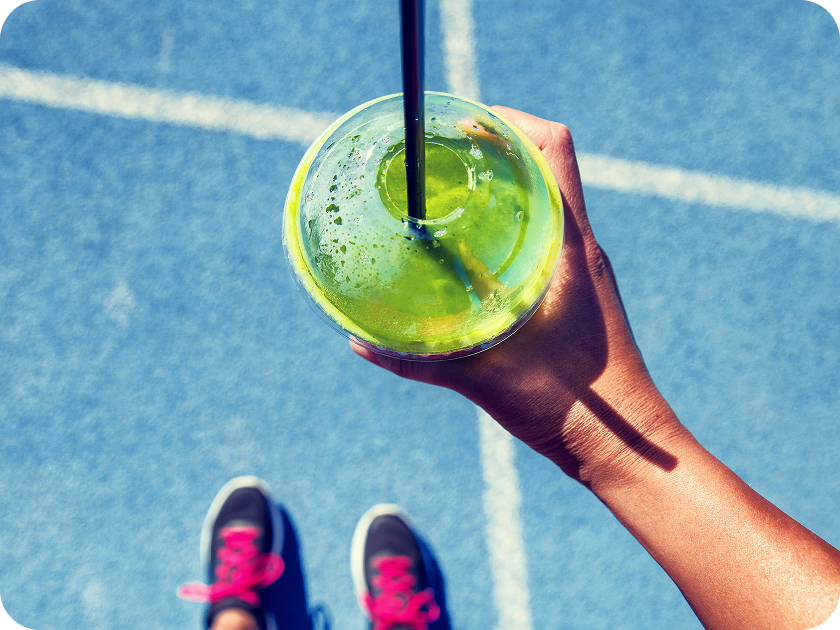 青いトラックで運動後のスムージーを持つ手とスニーカー。