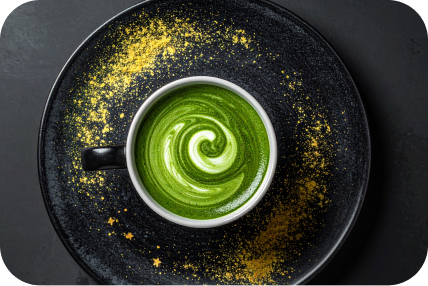 黒い皿に金粉と渦巻きラテアートが施された抹茶ラテのカップ。