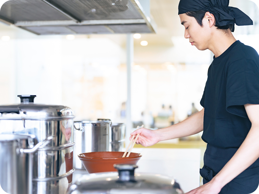 厨房で箸を使い調理をする若い男性シェフ。
