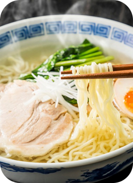 湯気を立てる澄んだスープのラーメン。チャーシュー、味玉、ネギ、青菜と、箸で持ち上げた麺。